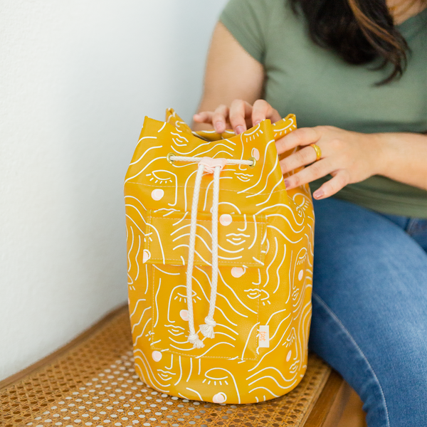 Woman in olive green shirt and jeans sitting next to a golden yellow bucket bag zen ladies talking out of turn