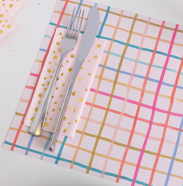 Colorful Table Setting with Checkered Placemat
A modern table setting featuring a pink placemat with a multicolor grid pattern in red, orange, gold, teal, and blue. A shiny fork and knife rest on pink napkins decorated with small gold geometric shapes, adding a festive and cheerful touch.
